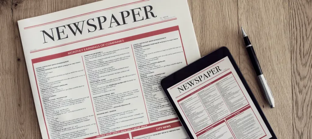 Gedruckte Zeitung und Tablet mit identischer Zeitungsausgabe nebeneinander auf einem Holztisch, symbolisch für Print-Abo und E-Paper.