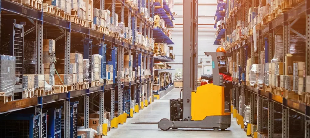 Gabelstaplerfahrer in einem großen Lager mit hohen Regalen und gestapelten Waren – Symbolbild für Abschaffung Umsatzsteuerlager.