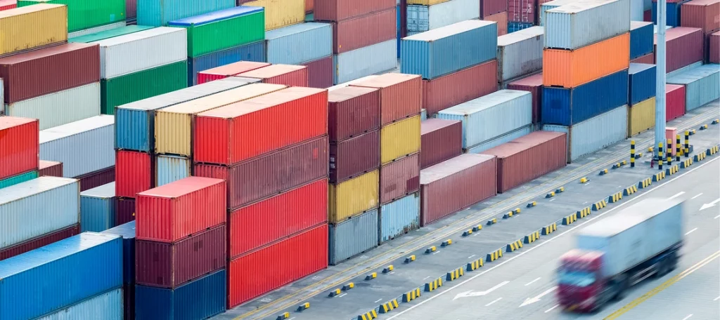 Gestapelte Schiffscontainer in einem Zolllager oder Containerterminal symbolisieren internationale Lieferketten, Einfuhr, Zollverfahren und steuerfreie Lieferungen vor der Einfuhr.