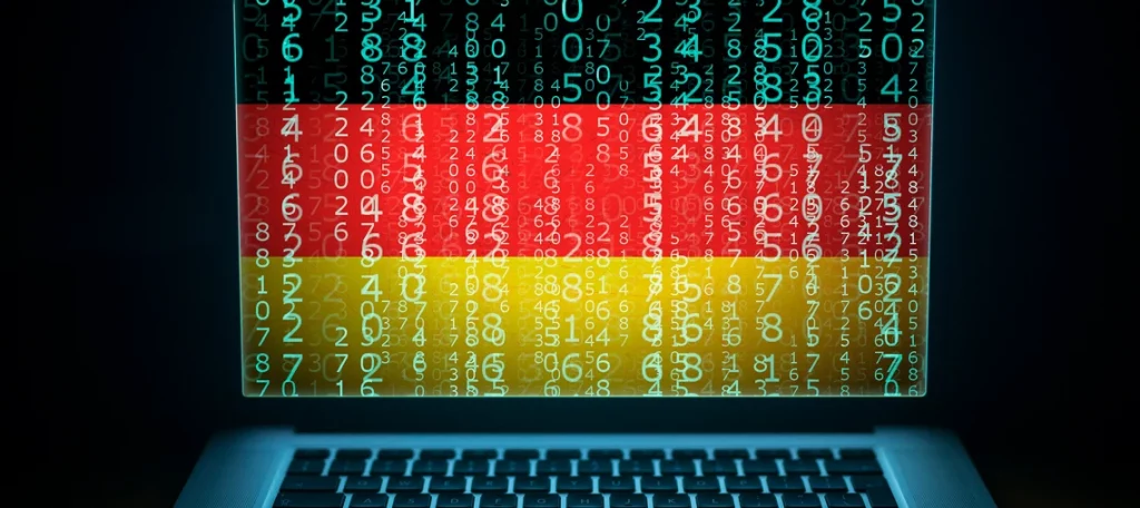E-Rechnung: Ein geöffneter Laptop, dessen Bildschirm die deutsche Nationalflagge zeigt, die von überlagernden Matrix-Zahlencodes aus türkis leuchtenden Ziffern gebildet wird, vor einem dunklen Hintergrund.