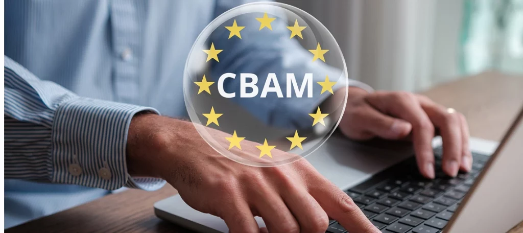 CO2-Grenzausgleich (CBAM) - Ein Nahaufnahme-Foto der Hände einer Person in einem blauen gestreiften Hemd, die auf einem Laptop tippen. Im Vordergrund schwebt eine transparente Blase mit dem weißen Akronym CBAM und einem Kreis aus gelben Sternen. Die Person sitzt an einem Holztisch.