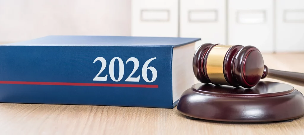 Blaues Gesetzbuch mit der Jahreszahl 2026 und rotem Unterstrich neben einem Richterhammer auf Holztisch, im Hintergrund Aktenschränke – Neues-zum-Jahressteuergesetz-2026