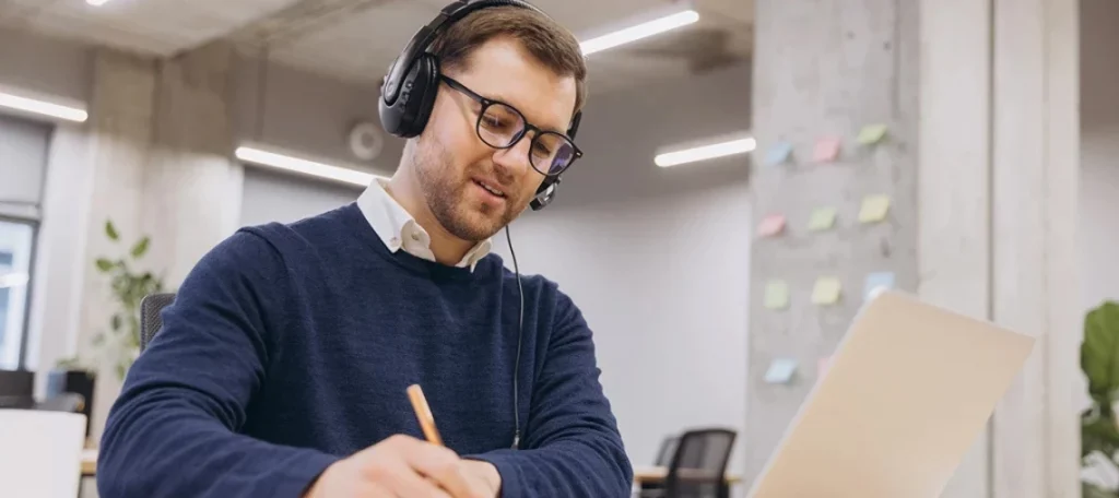 Wegfall des FernUSG: Mann mit Headset nimmt Notizen während Online-Fernunterricht am Laptop im Büro